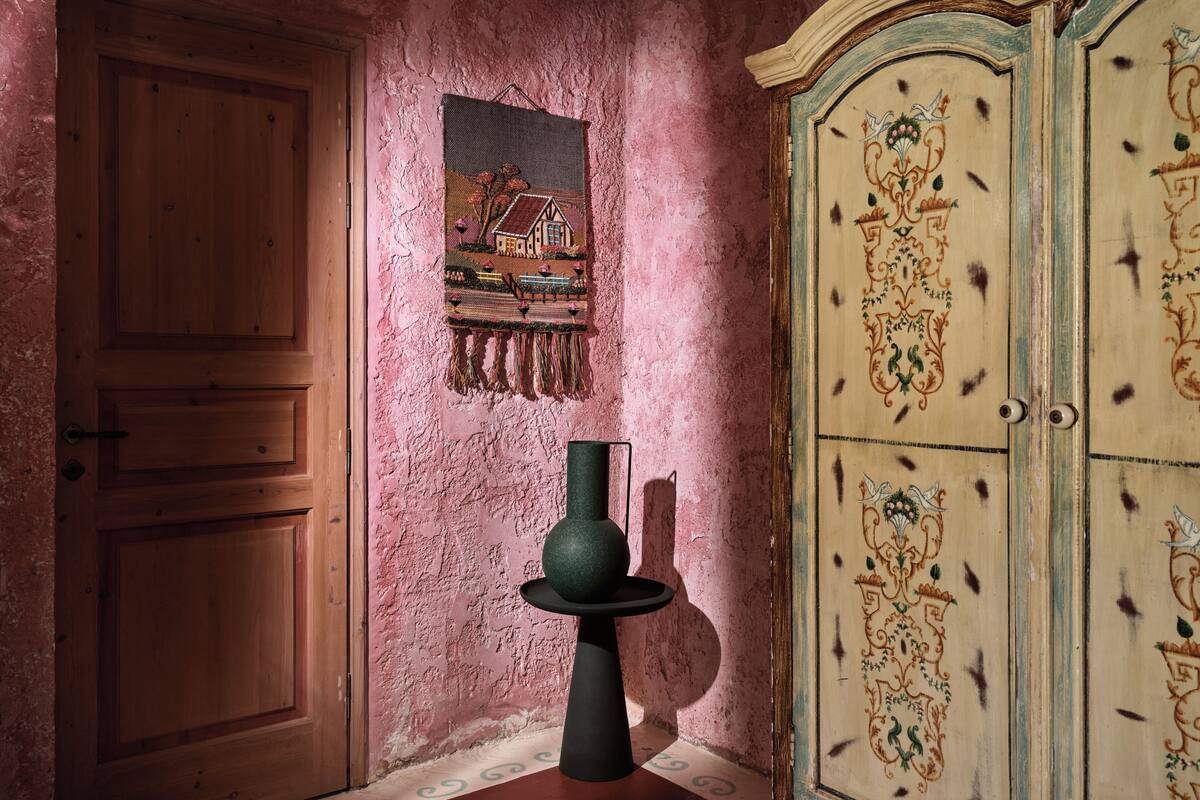 A room with a wooden door, a wall-mounted tapestry, and a decorative cabinet.