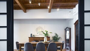 A dining area with a wooden table, four chairs, a vase with a plant, and a cabinet with books.