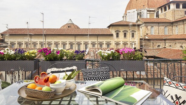 A terrace with a table set for a meal, a basket of fruits, and a view of a historic building with a dome.