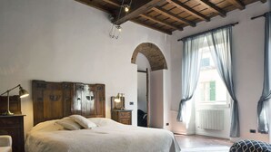 A bedroom with a wooden headboard, a bed with a white bedspread, a nightstand with a lamp, a dresser, and a window with curtains.