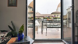 A room with a view of a courtyard, a metal bench, a potted plant, and a framed picture on the wall.
