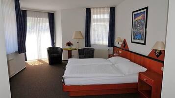 Habitación de hotel con cama, dos sillas, un escritorio, lámparas y un cuadro en la pared.