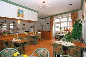 Uma área de refeições com mesas e cadeiras de madeira, um espaço de bar e uma grande janela com cortinas.