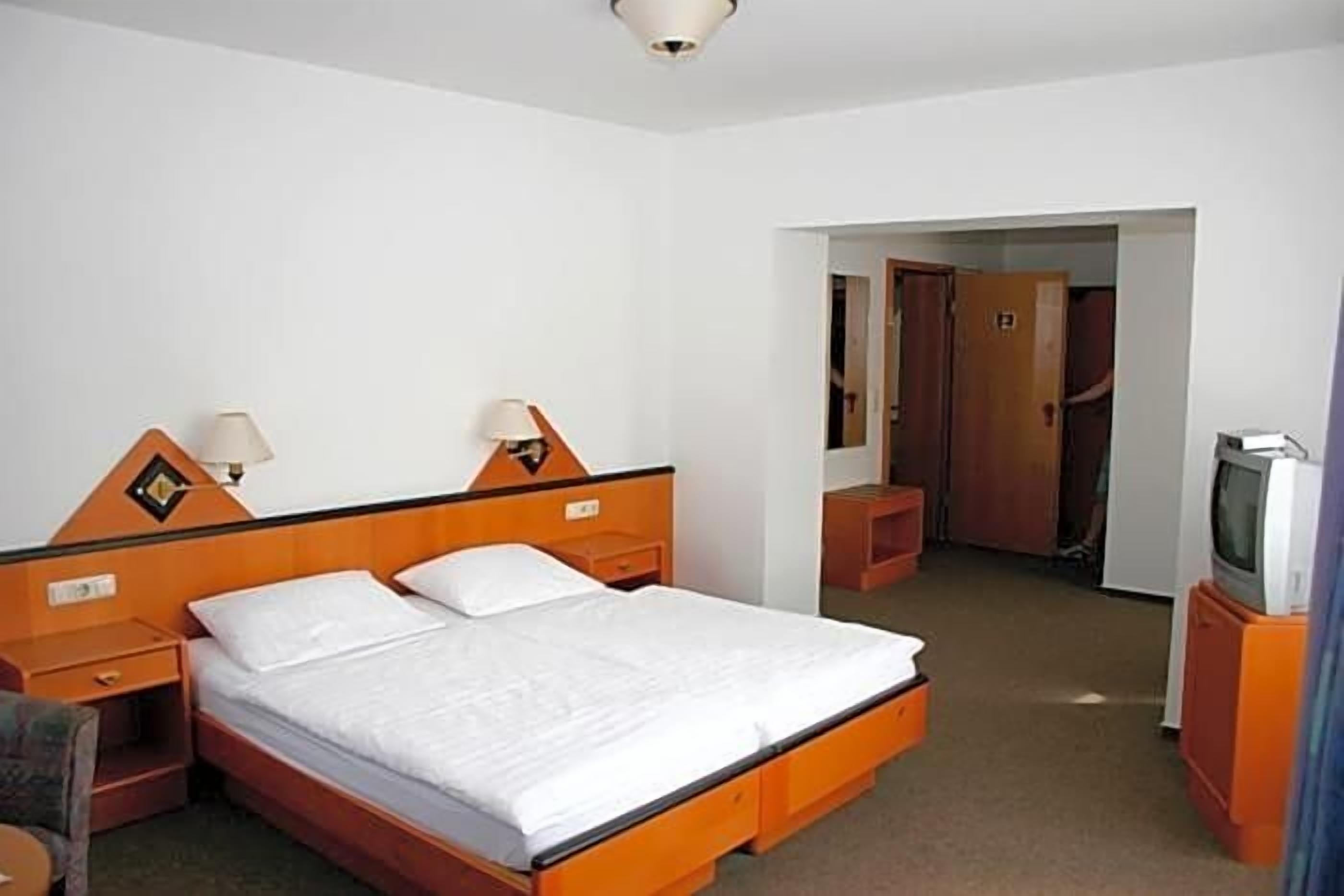 Una habitación de hotel con una cama individual, mesitas de noche, un televisor y un armario.