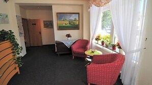 A room with a bed, a red armchair, a small table, a window with curtains, and a painting on the wall.