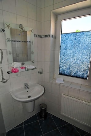 Casa de banho com lavatório branco, espelho, janela com vista azul texturizada e radiador.