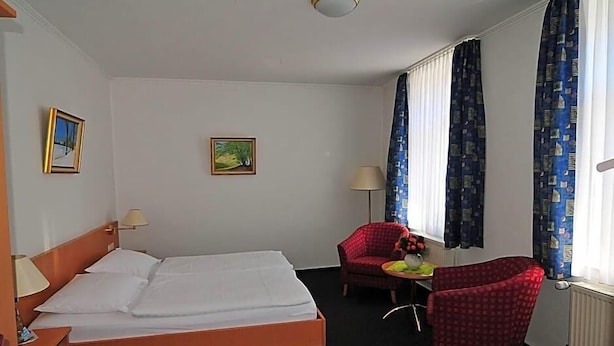 A hotel room with a bed, two chairs, a table with a vase, and curtains.