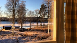A window view of a landscape with trees, a body of water, and a distant hill. - Vildmarks Lodge (Ytterhogdal)