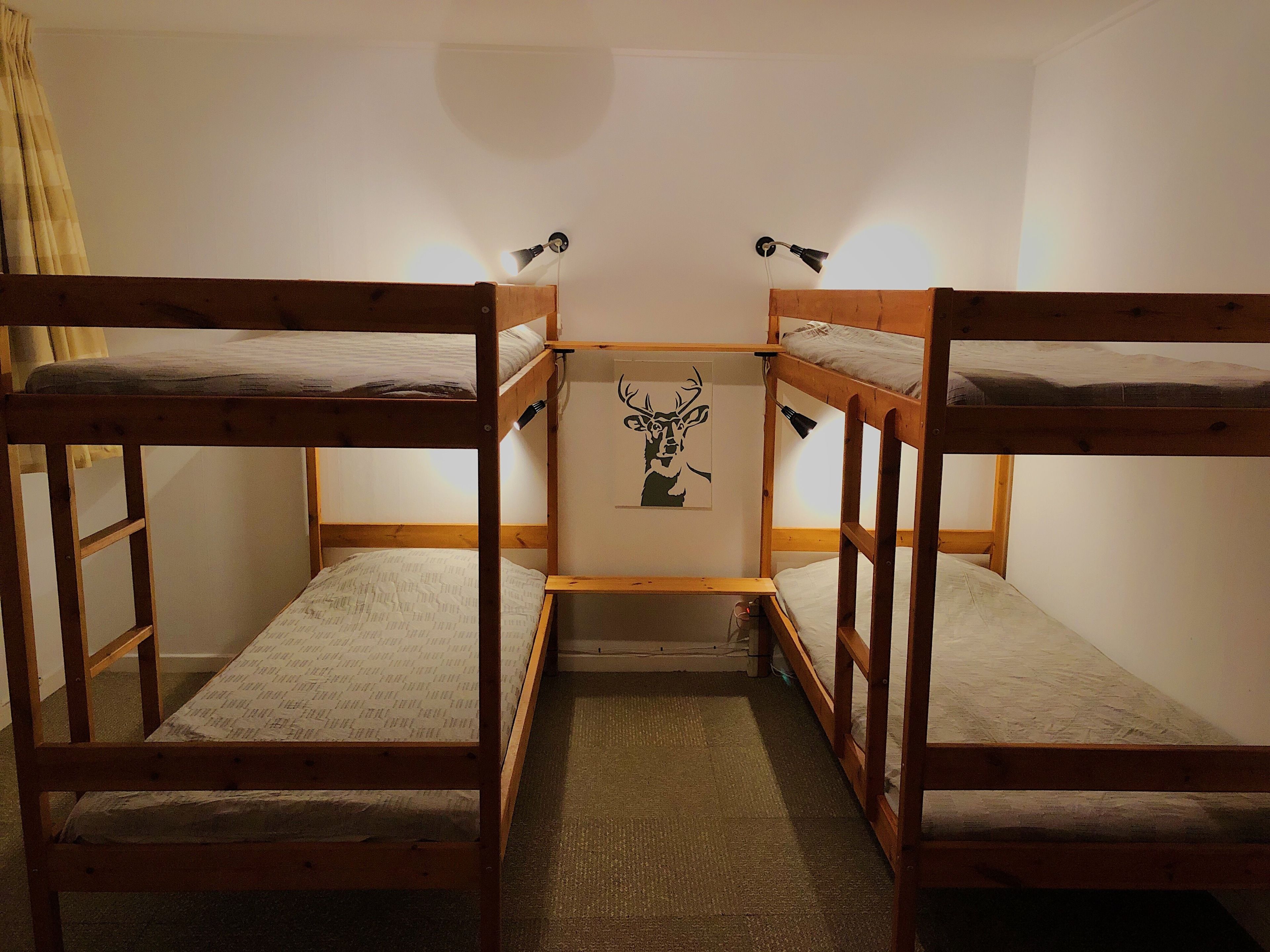 Une chambre avec un lit superposé, deux lits, une petite table et une lampe fixée au mur.