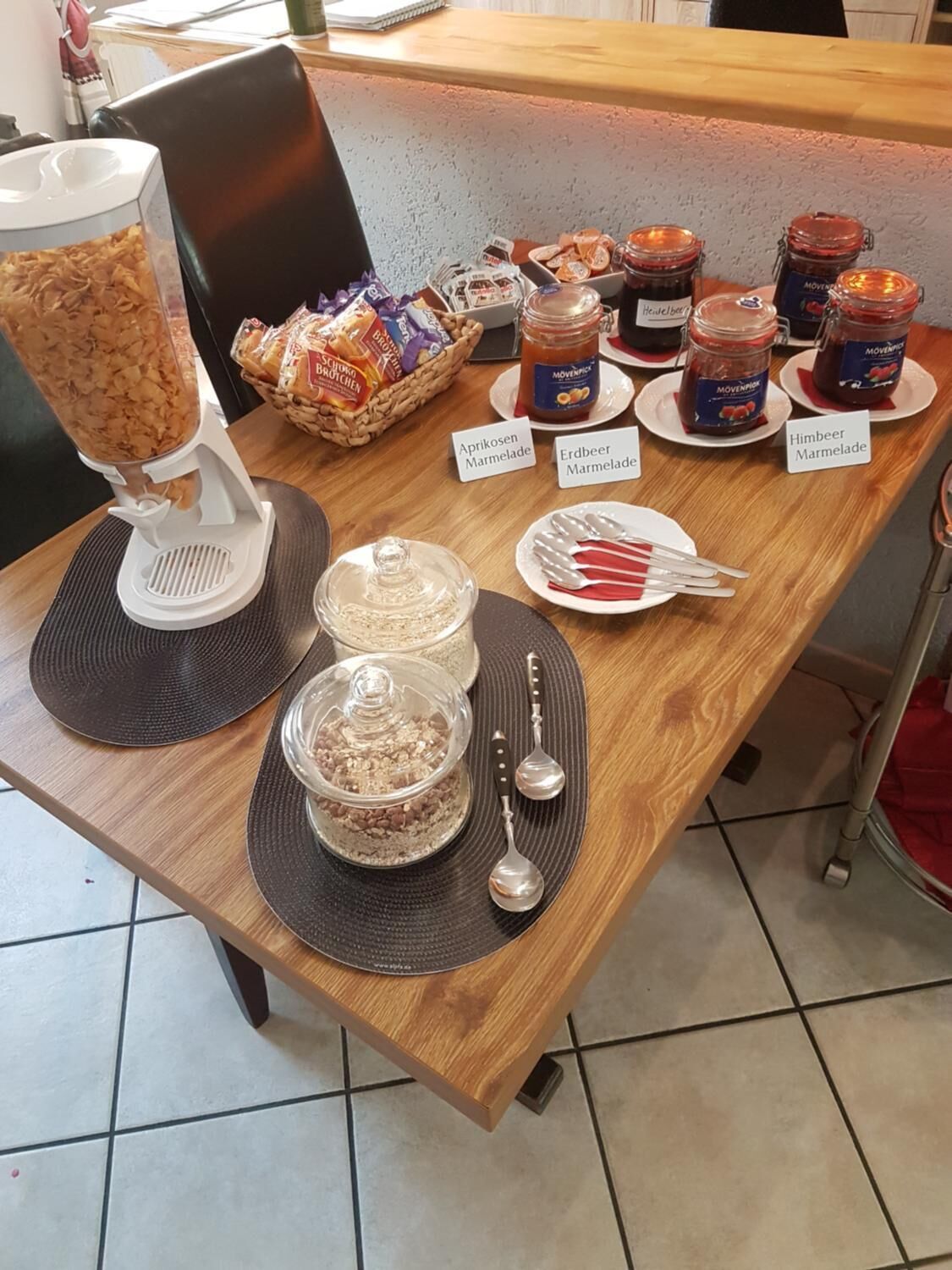 Ein Buffet mit verschiedenen Speisen und Beilagen, darunter Gläser mit 'Aprikosen Marmelade' und 'Himbeer Marmelade'.