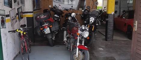 Un garaje para motocicletas con varias motocicletas estacionadas, una bicicleta y diversas herramientas y equipos en estantes.