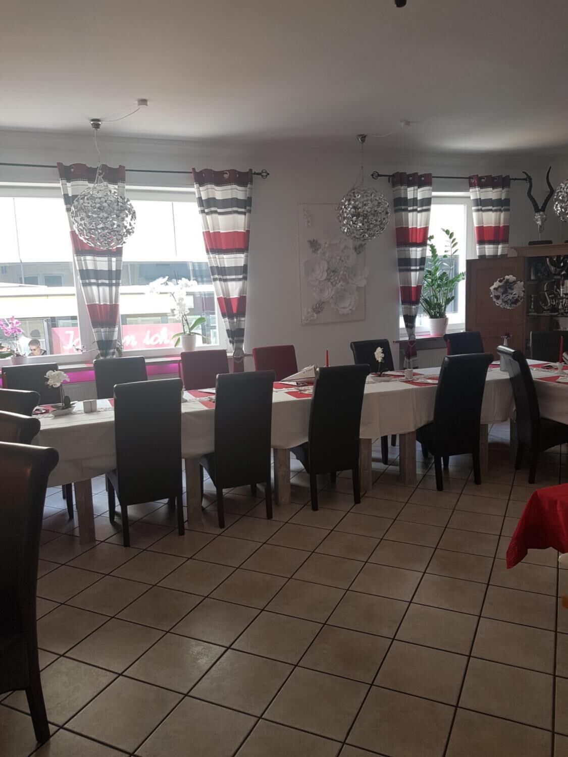 A dining area with multiple tables and chairs, large windows with striped curtains, and a tiled floor.