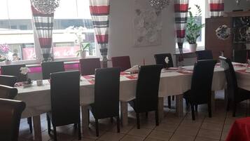 A dining area with multiple tables and chairs, large windows with striped curtains, and a tiled floor.