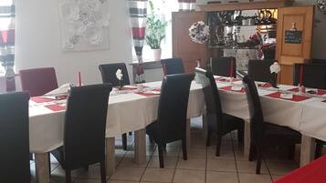 A dining area with a tiled floor, white tablecloths, and black chairs.
