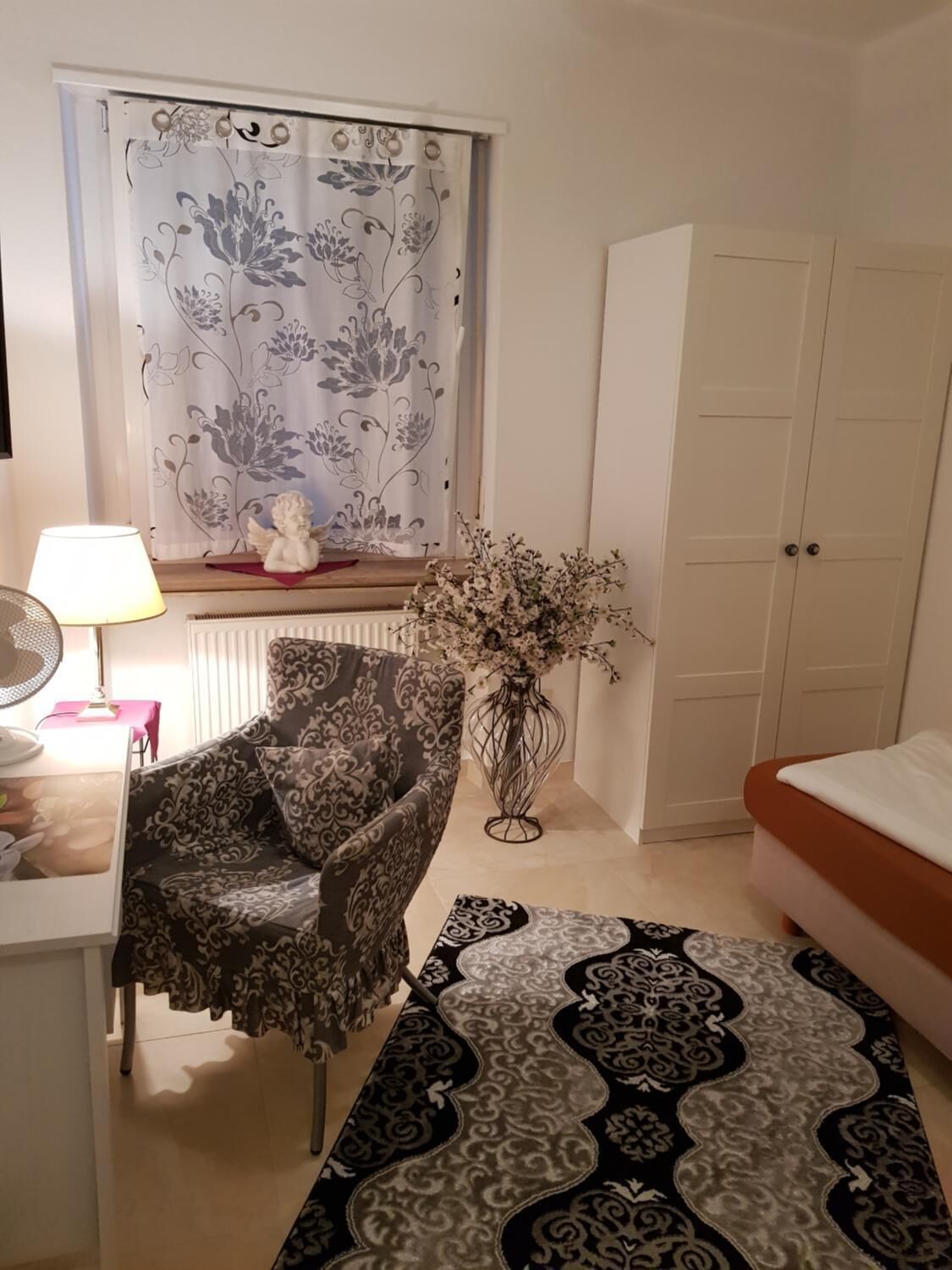 Un dormitori amb un sofà estampat, una taula de nit amb una làmpada, un vas decoratiu i una catifa amb dibuixos.