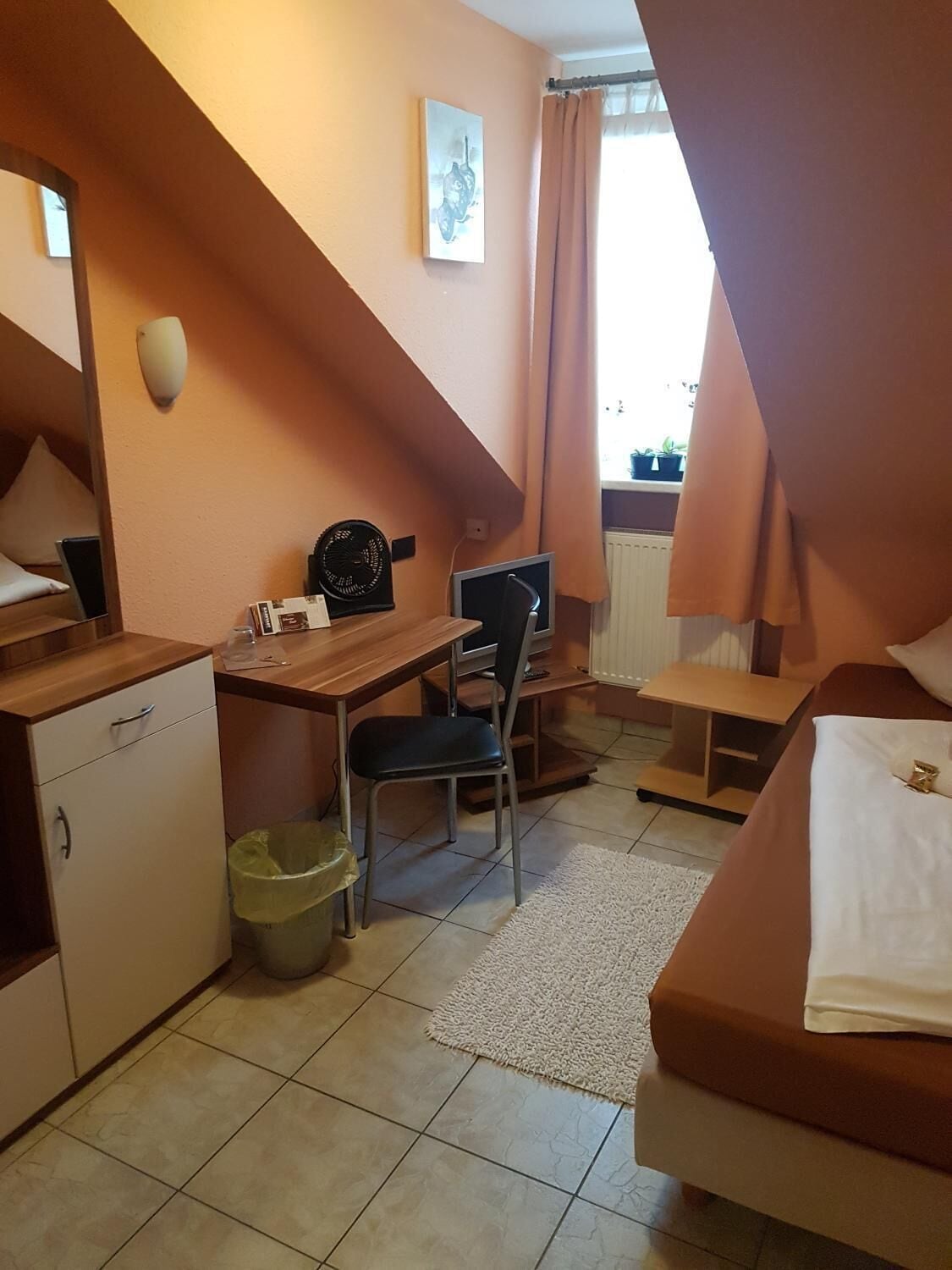 Habitación de hotel pequeña con cama, escritorio, silla y una kitchenette.