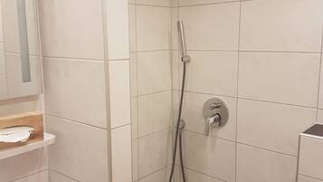 A small, tiled shower area with a handheld showerhead and a wall-mounted faucet.
