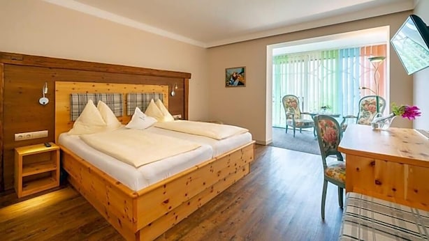 Una cama doble con cabecera de madera, una mesita de noche y una silla con cojín estampado de flores.