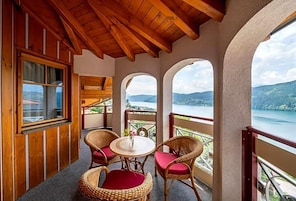 Varanda de madeira com cadeiras de vime e uma mesa, com vista para um lago e montanhas.