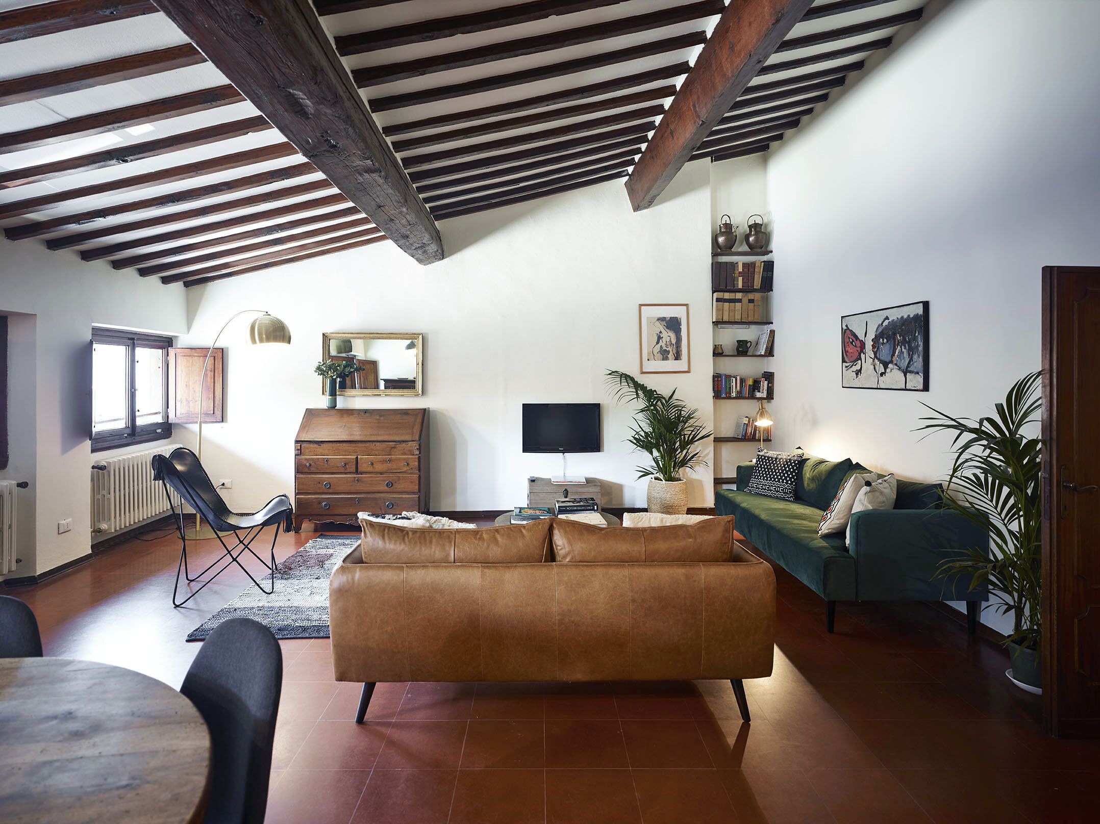 A living room with a brown sofa, a green couch, a wooden cabinet, a TV, and a bookshelf.