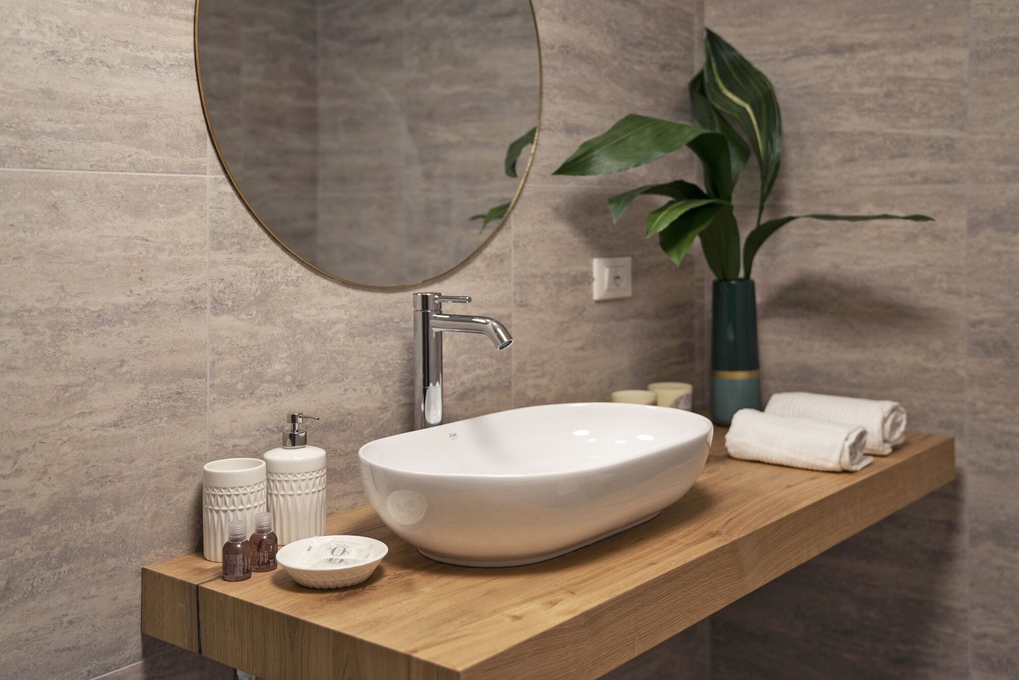A modern bathroom with a large oval sink, a mirror, and a potted plant.
