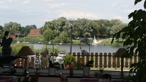 A view from a balcony overlooking a river with boats, trees, and a statue. - Hotel Seeblick Garni (Gartow)
