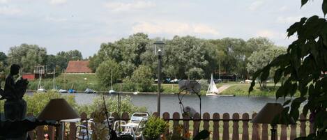 A view from a balcony overlooking a river with boats, trees, and a statue.