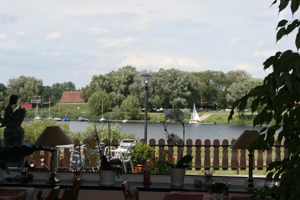 A view from a balcony overlooking a river with boats, trees, and a statue.