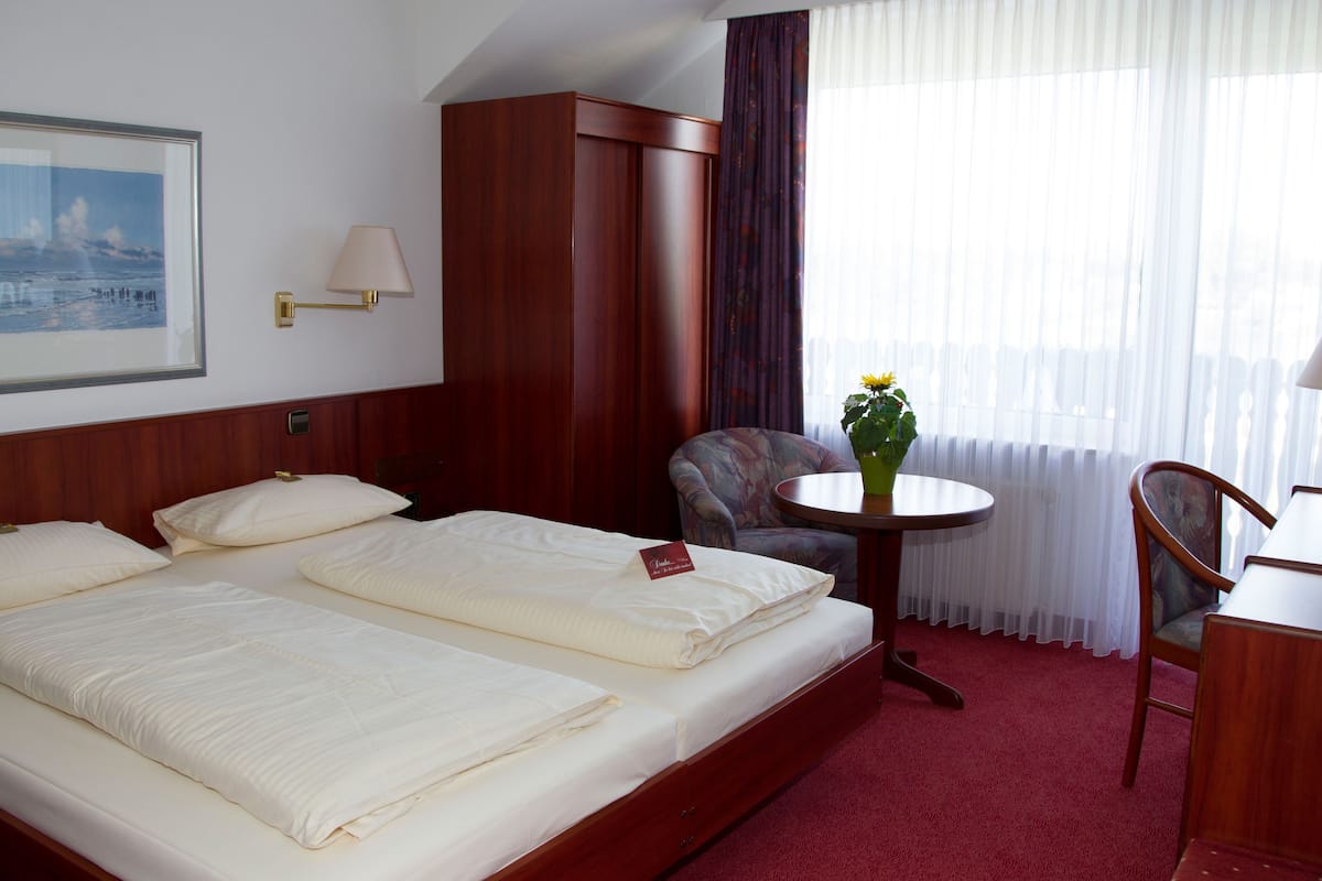 Habitación de hotel con dos camas, un armario de madera, un escritorio con silla y una ventana con cortinas.