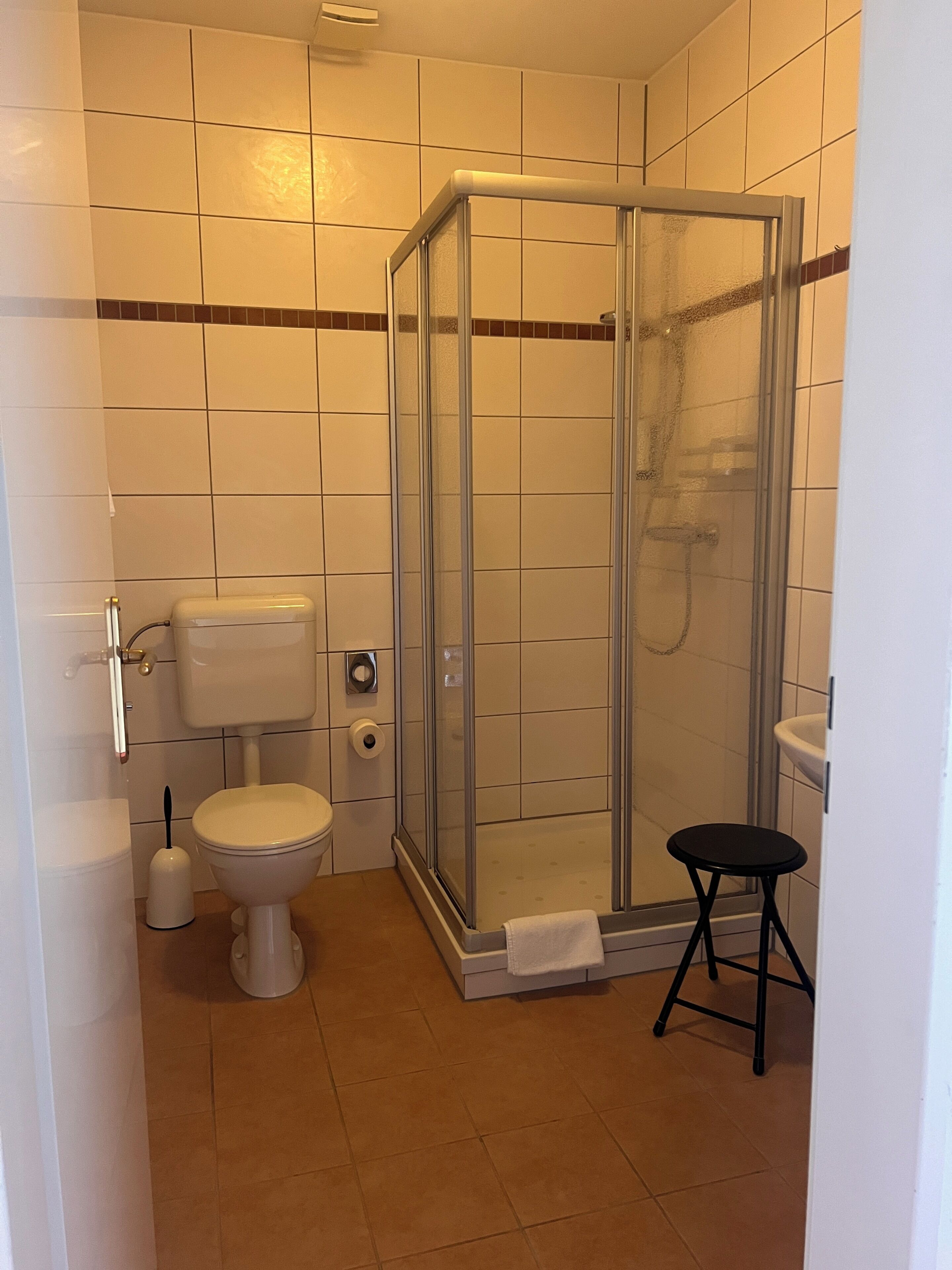 Une salle de bain avec une douche à parois de verre, des toilettes et un petit tabouret.