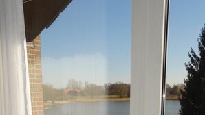 A room with a view of a lake, a white chair outside, and a radiator on the wall. - Hotel Seeblick Garni (Gartow)