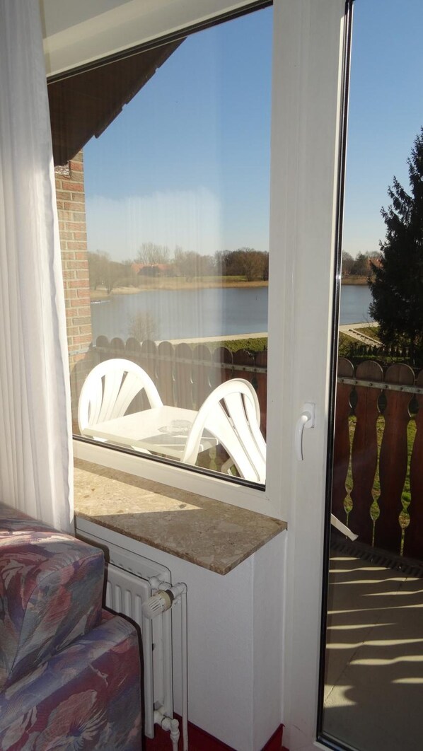 A room with a view of a lake, a white chair outside, and a radiator on the wall. - Hotel Seeblick Garni (Gartow)