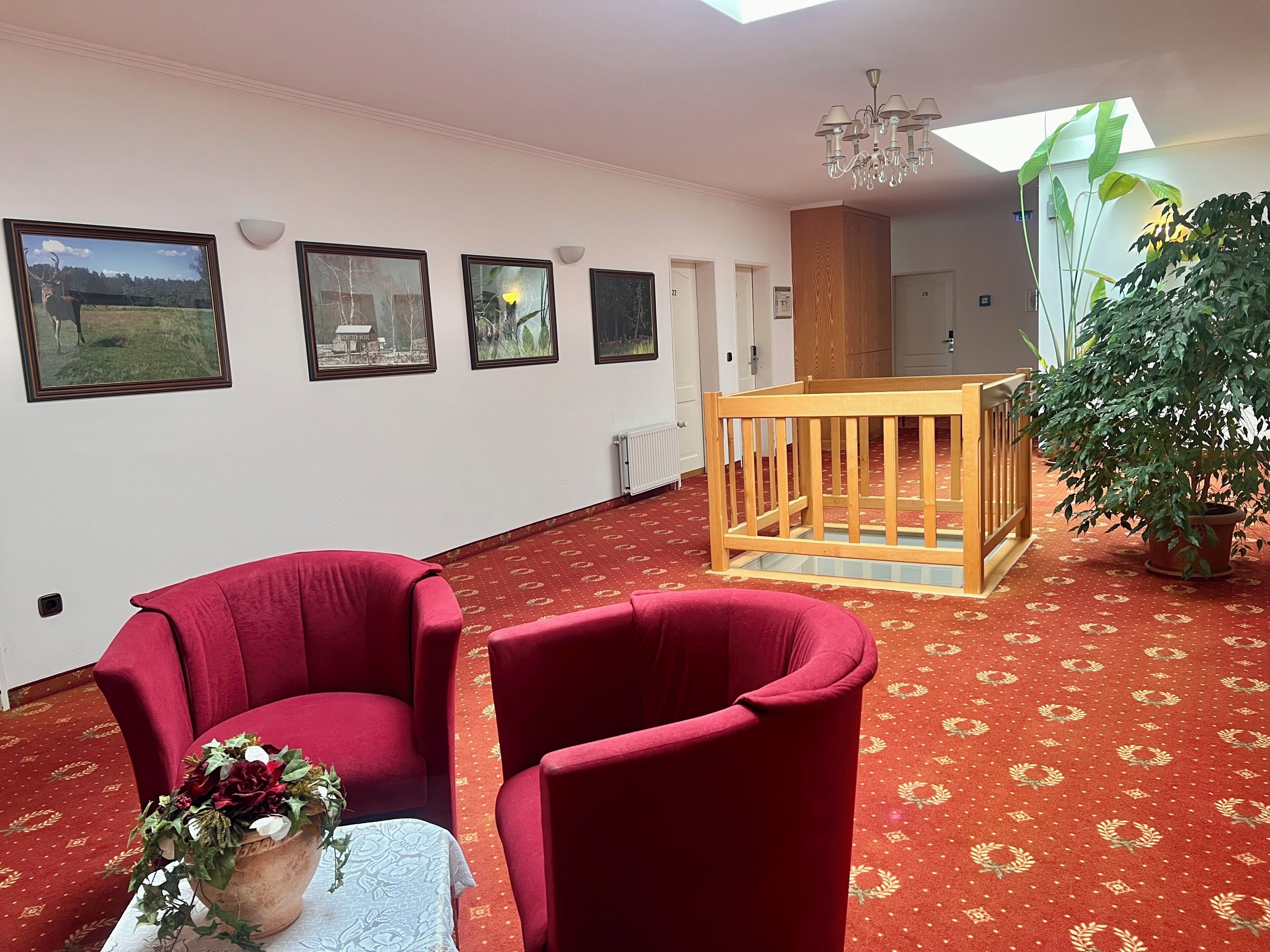 A room with a red carpet, a wooden crib, a potted plant, and framed pictures on the wall.