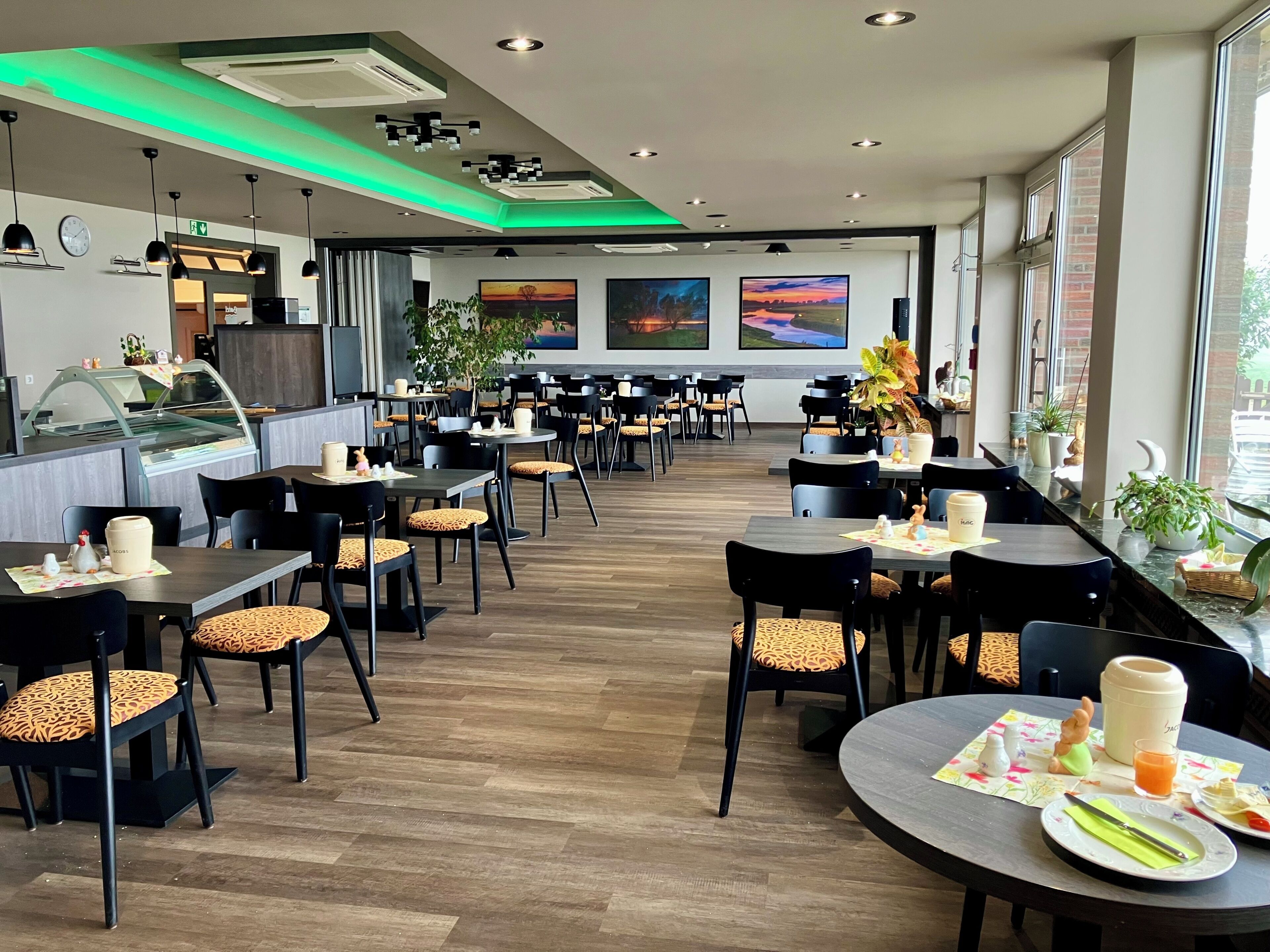 Un restaurant avec plusieurs tables et chaises, un comptoir avec une vitrine, et des œuvres d’art accrochées aux murs.