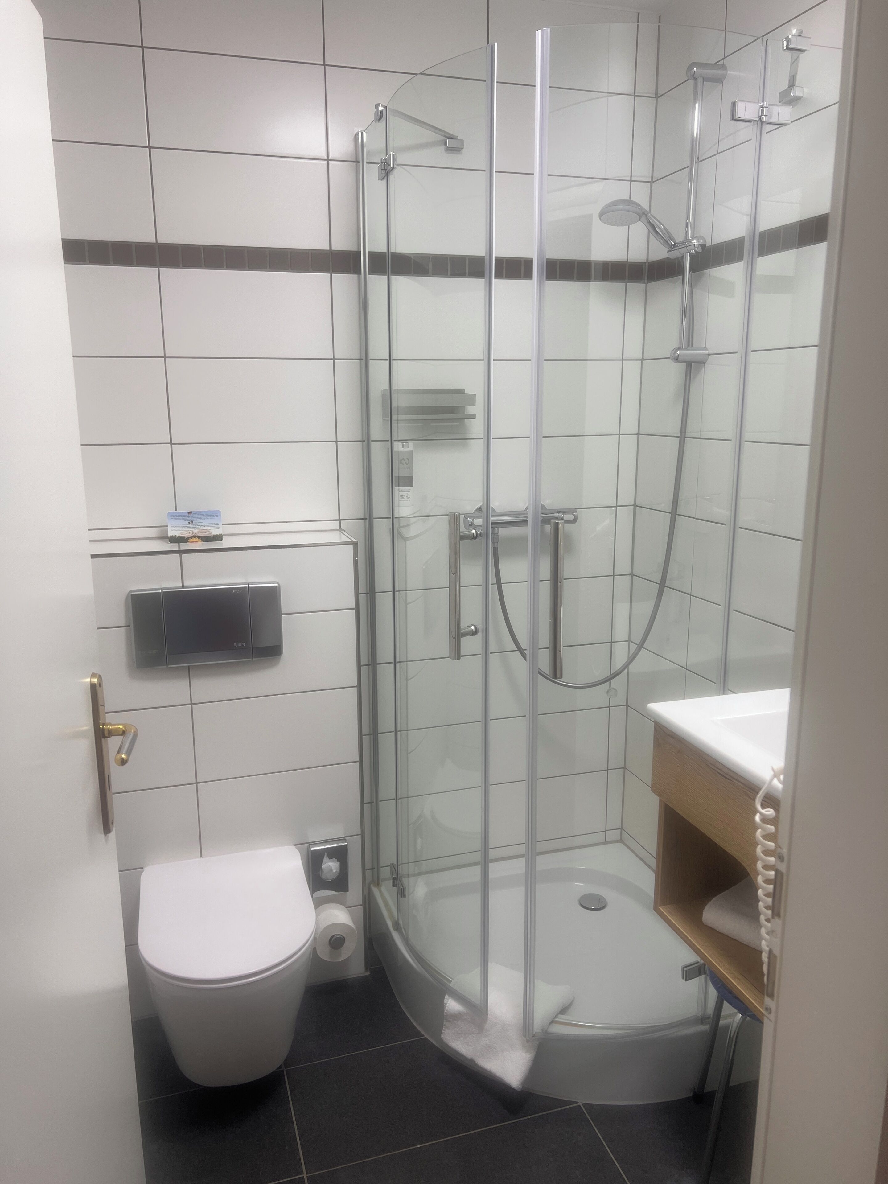 Un baño moderno con ducha envuelta en vidrio, inodoro y lavabo con tocador de madera.