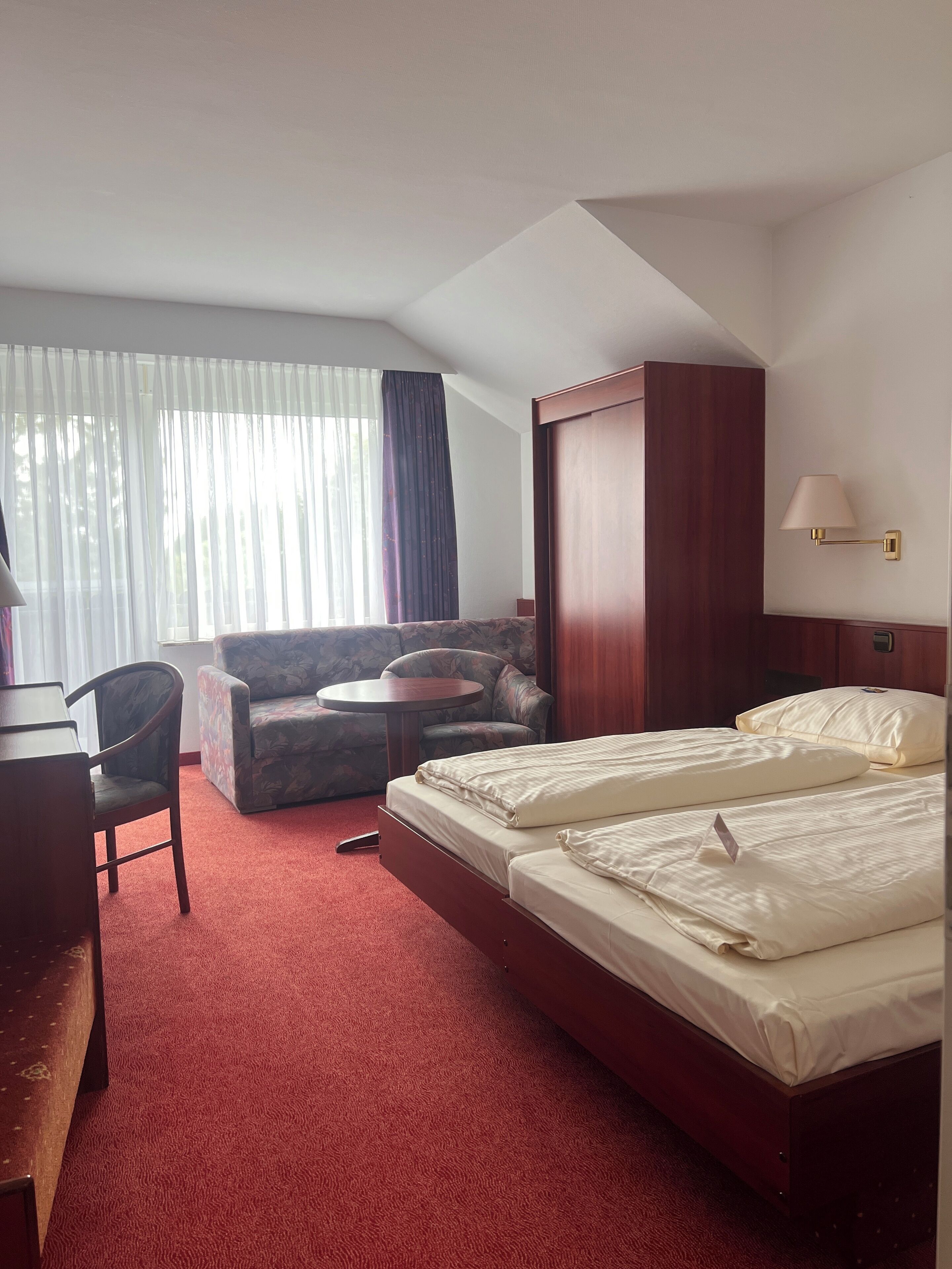 A hotel room with a bed, a desk, a chair, a sofa, and a window with curtains.