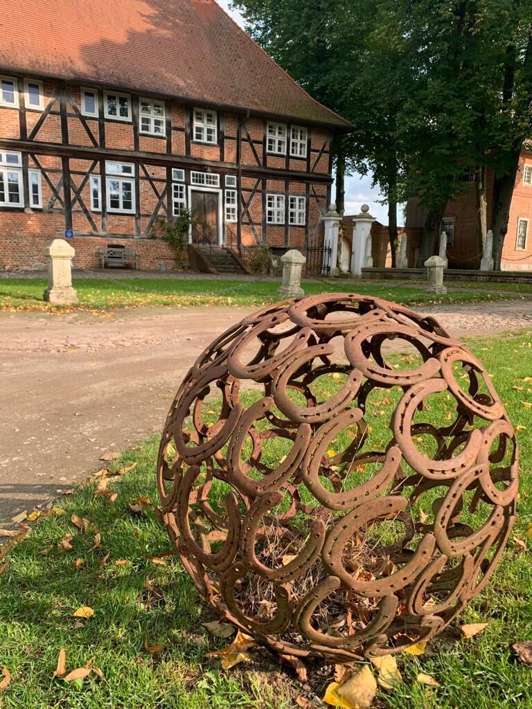 A metal sculpture of interlinked horseshoes in a grassy area with a traditional building in the background.