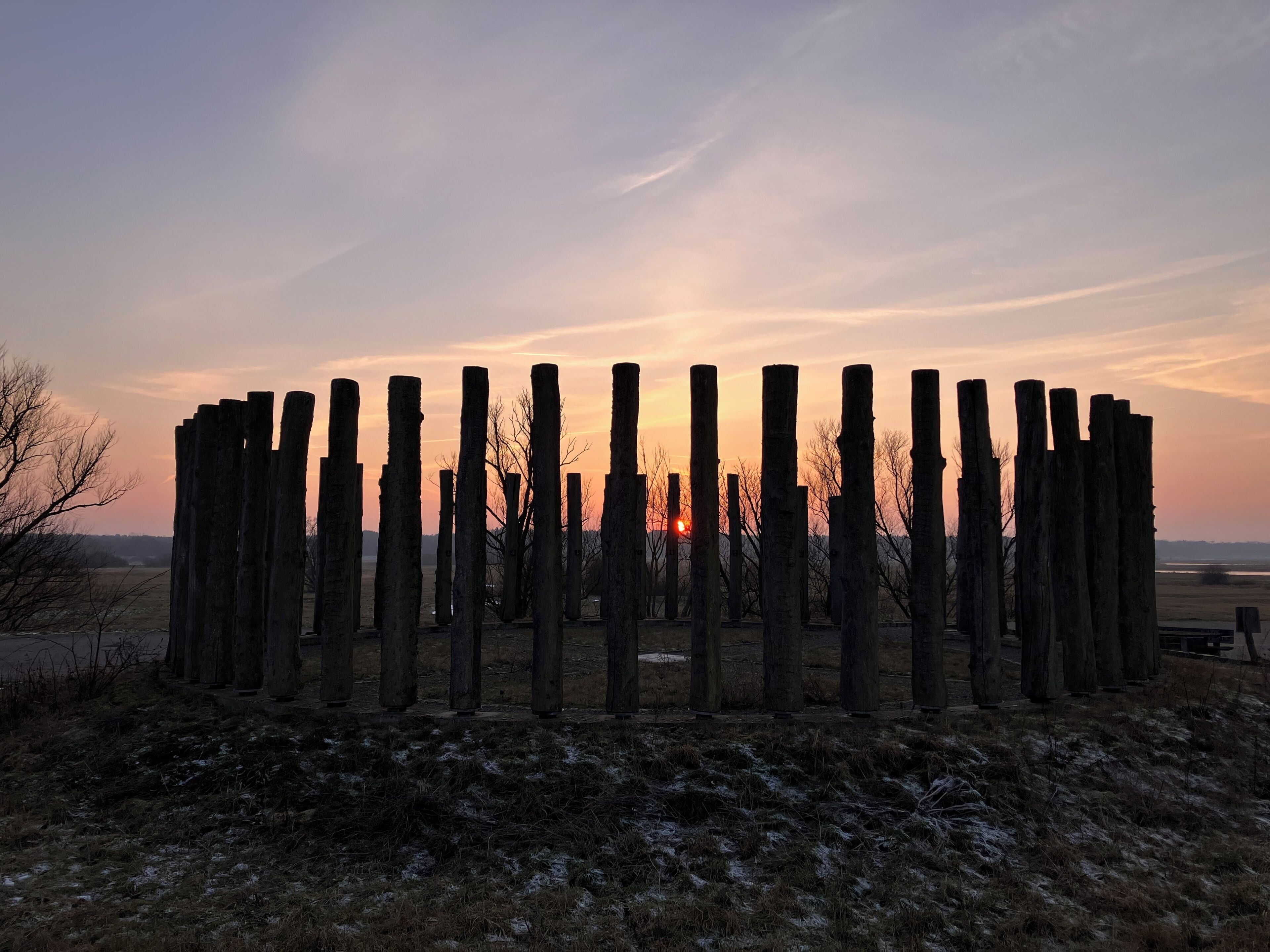 Rivissä on puisia tolppia pellolla, ja taustalla näkyy auringonlasku.