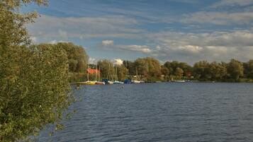 A calm lake with boats docked on the shore, surrounded by trees and buildings.