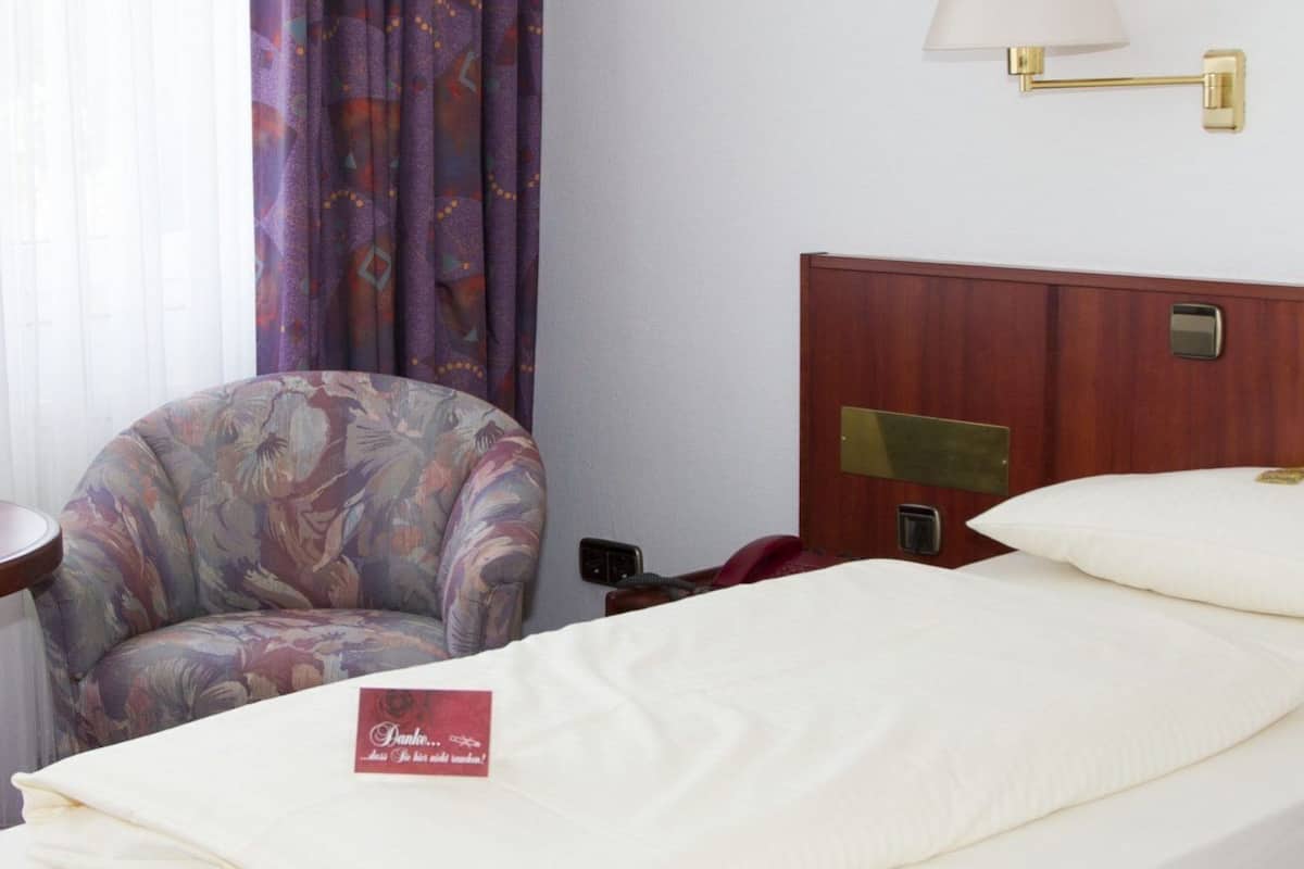 Habitación de hotel con cama, una silla, una lámpara y un panel de control en la pared.