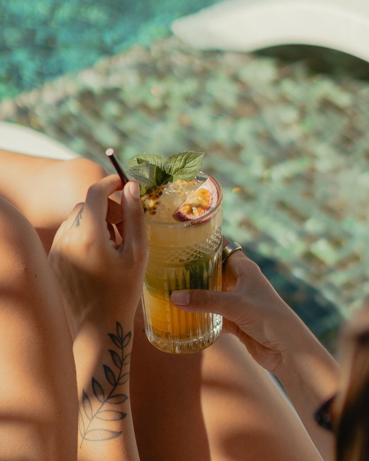 Iemand houdt een glas met een drankje vast, versierd met een stuk fruit en een muntblaadje.