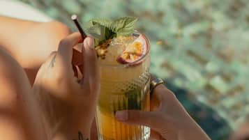 A person holding a glass with a drink garnished with a slice of fruit and a mint leaf.