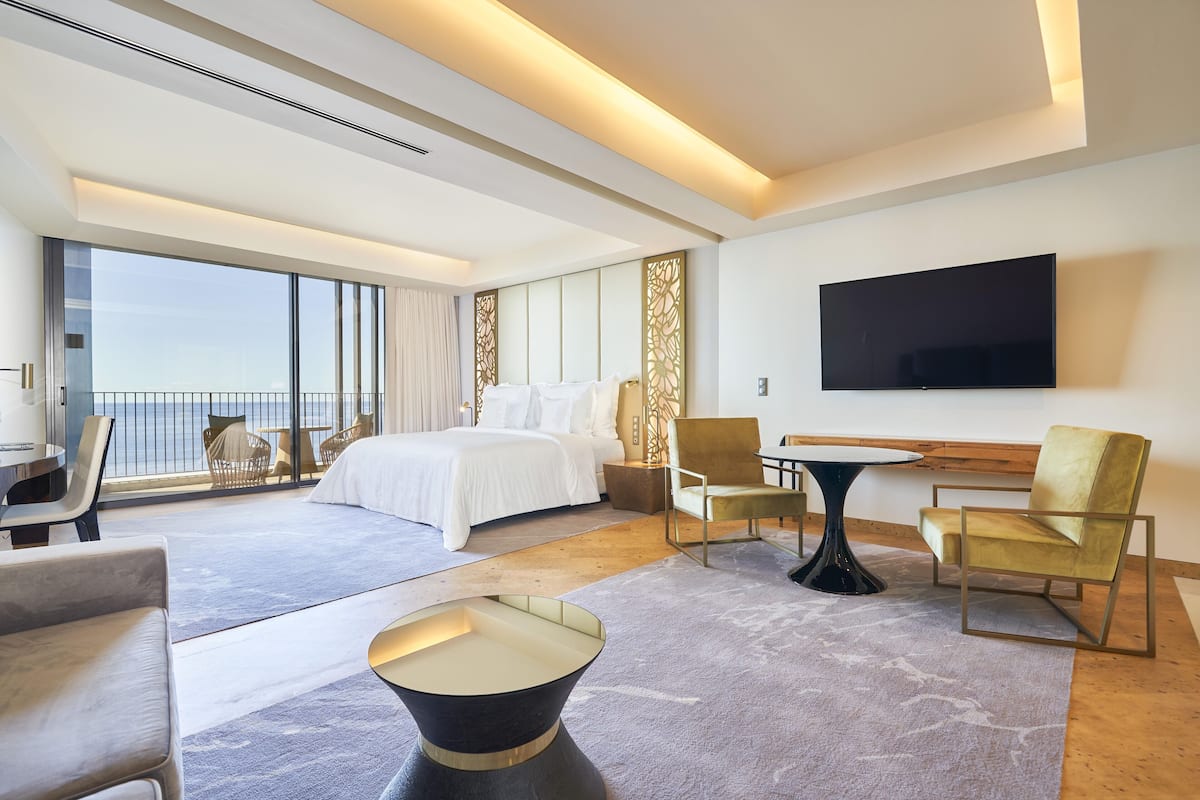 A modern hotel room with a large bed, a TV, and a balcony with a view.
