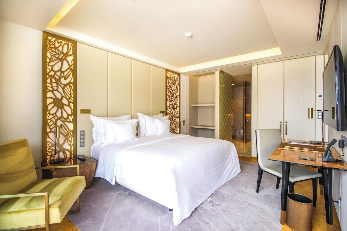 A modern hotel room with a large bed, a desk with a chair, and a television.