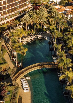 Vista aérea de un resort con piscina central, rodeado de palmeras y zonas de descanso.