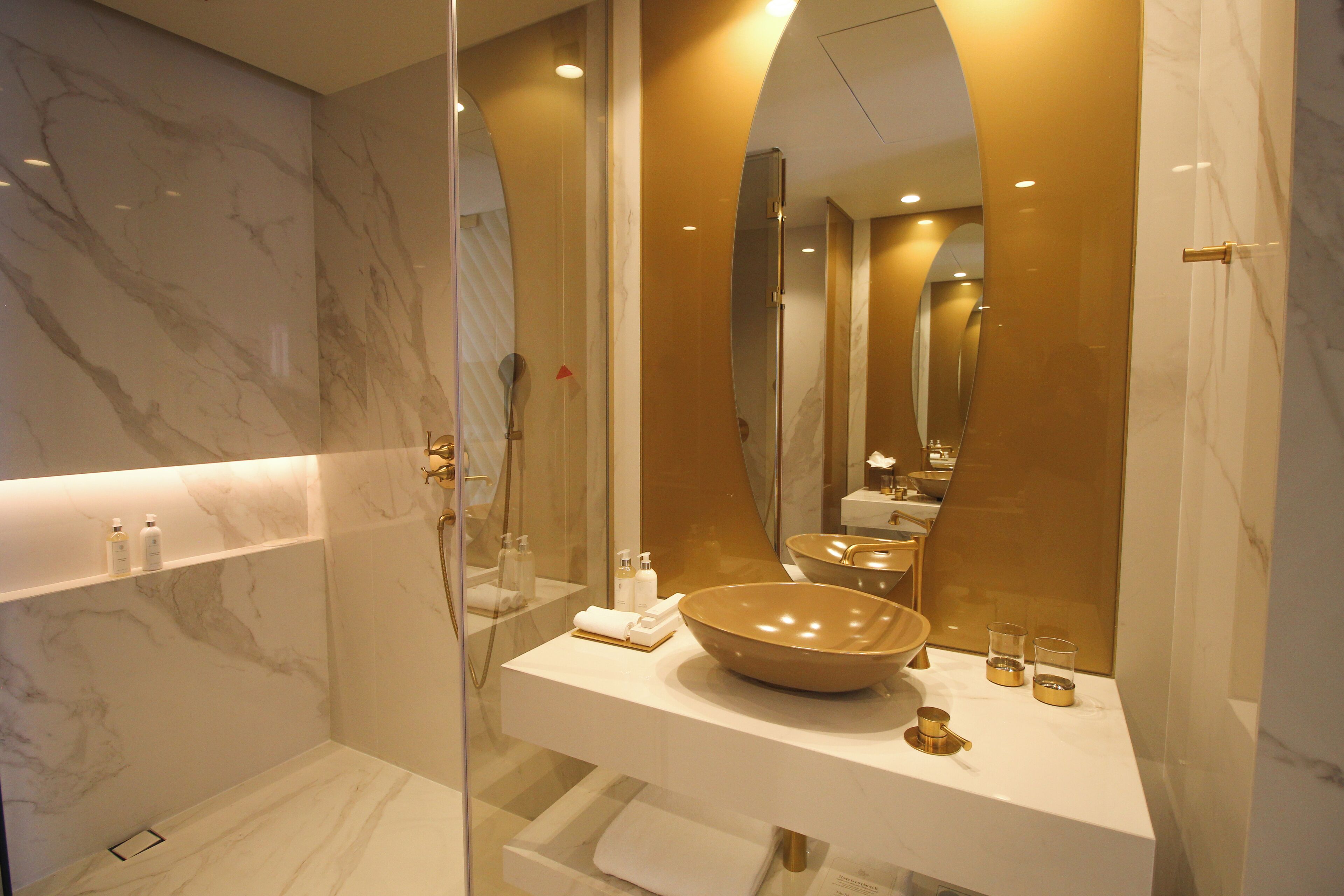 A modern bathroom with a large mirror, a marble vanity, and a glass-enclosed shower.