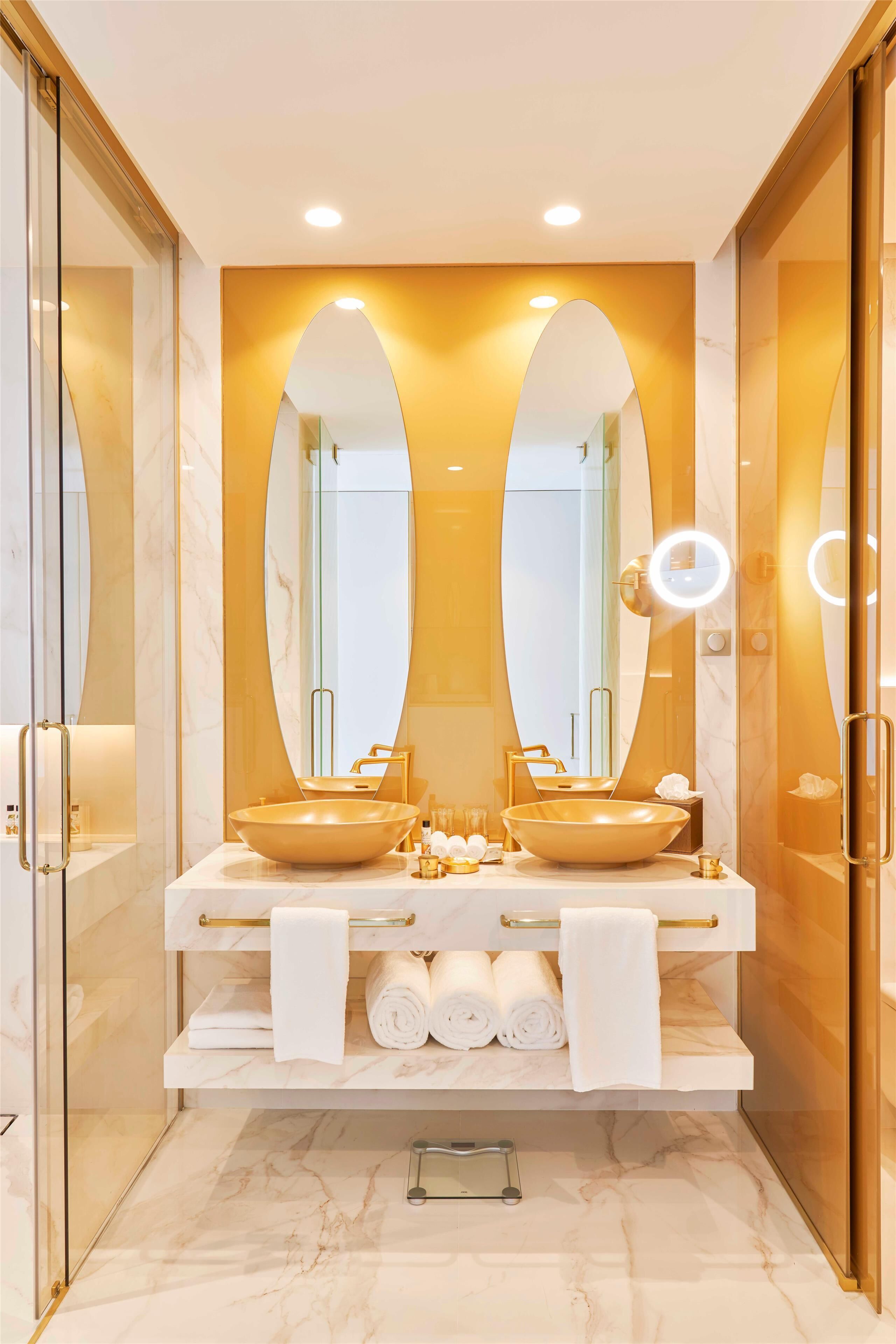 A modern bathroom with two sinks, a large mirror, and a vanity with towels.
