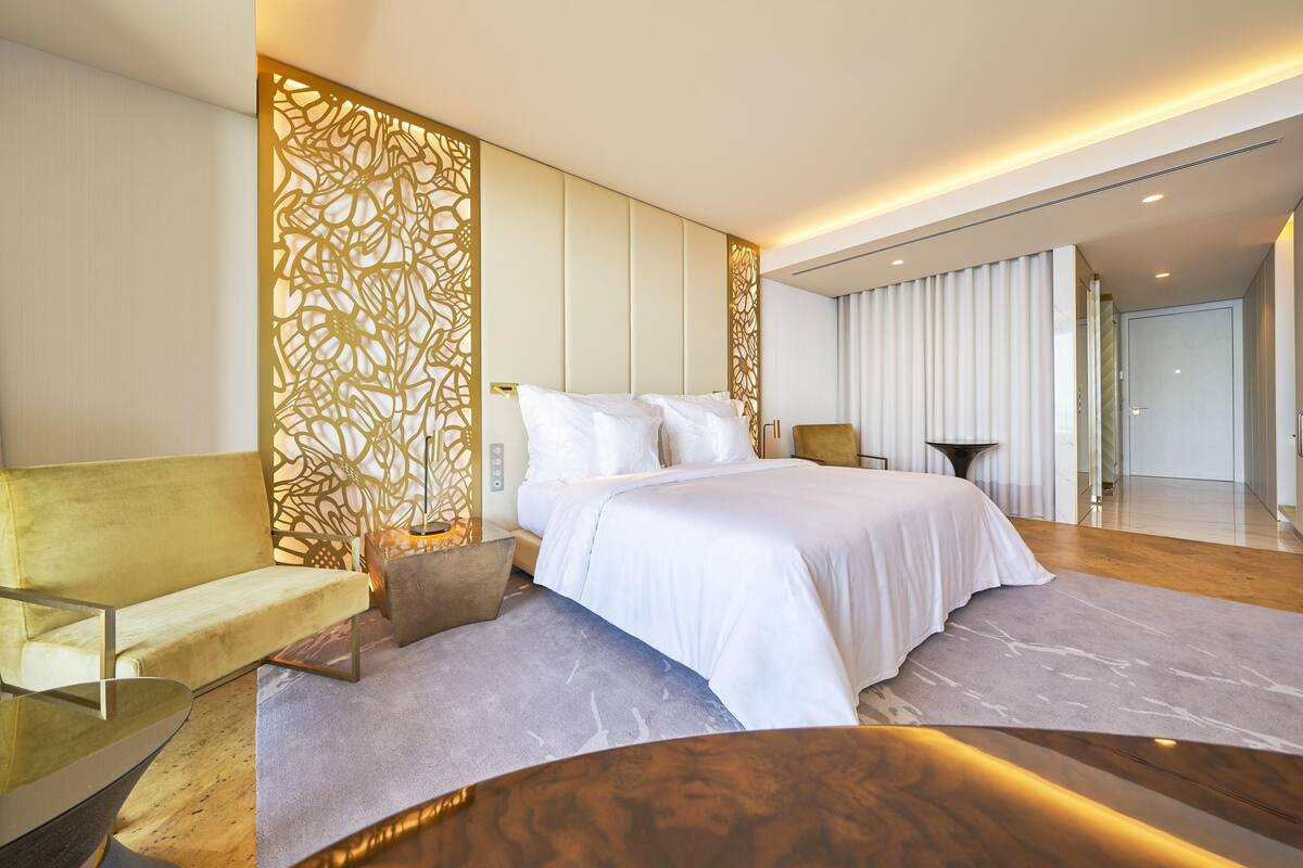 A modern hotel room with a large bed, a sofa, a small table, and a decorative wall panel.