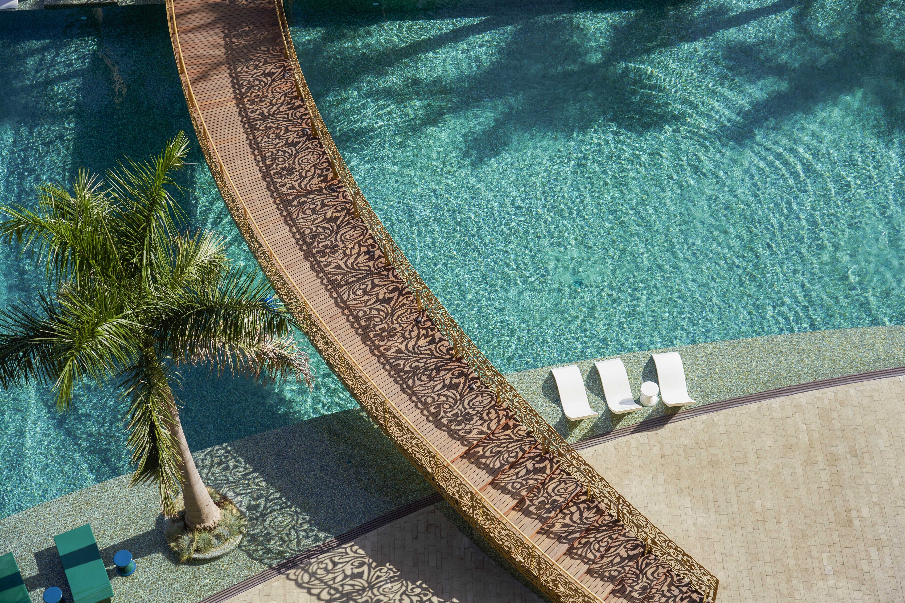 An aerial view of a pool area with a decorative pathway, lounge chairs, and a palm tree.