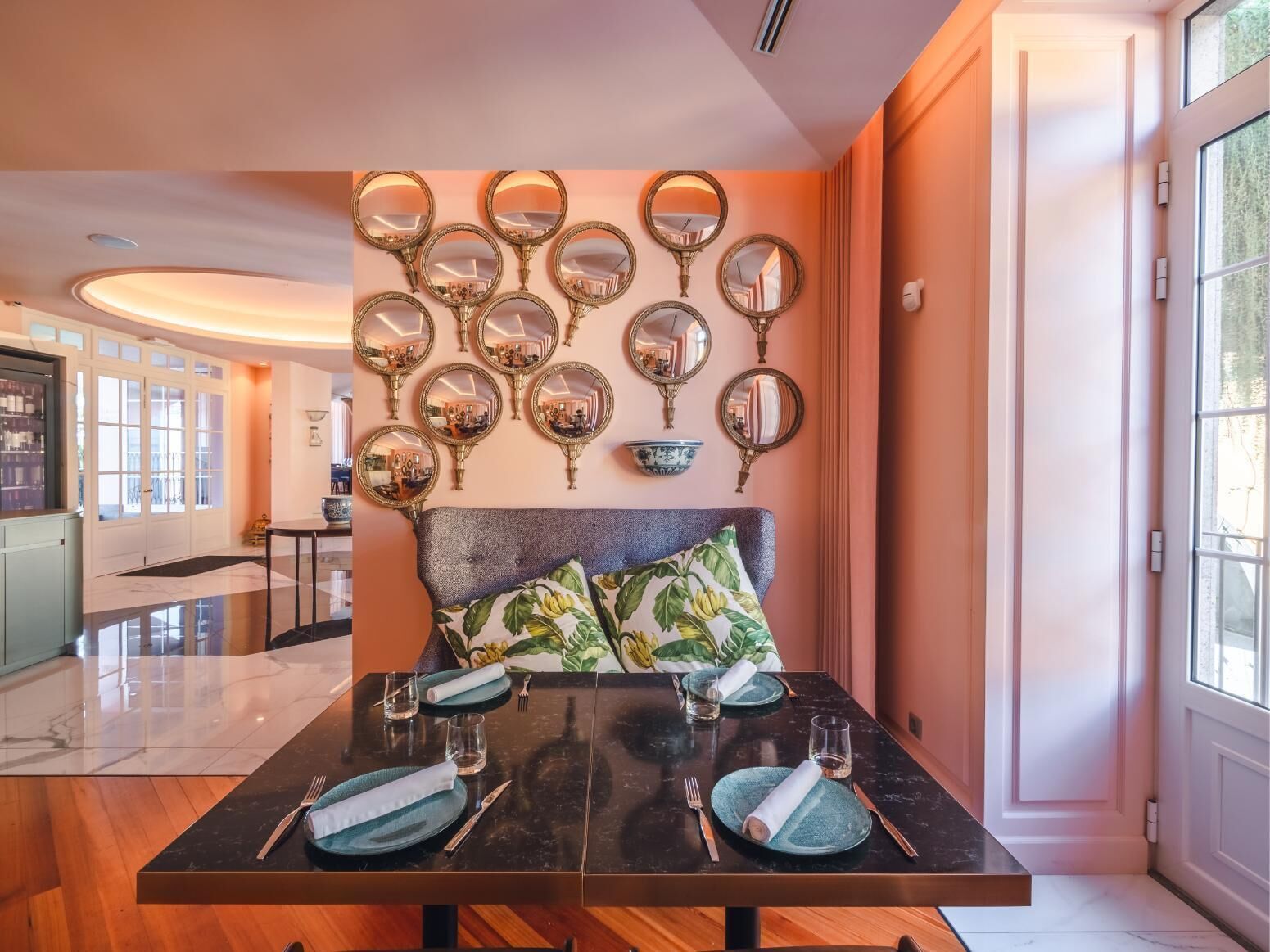 Un coin repas avec une table en marbre noir, dressée pour quatre personnes, entourée d’un mur recouvert de miroirs décoratifs.